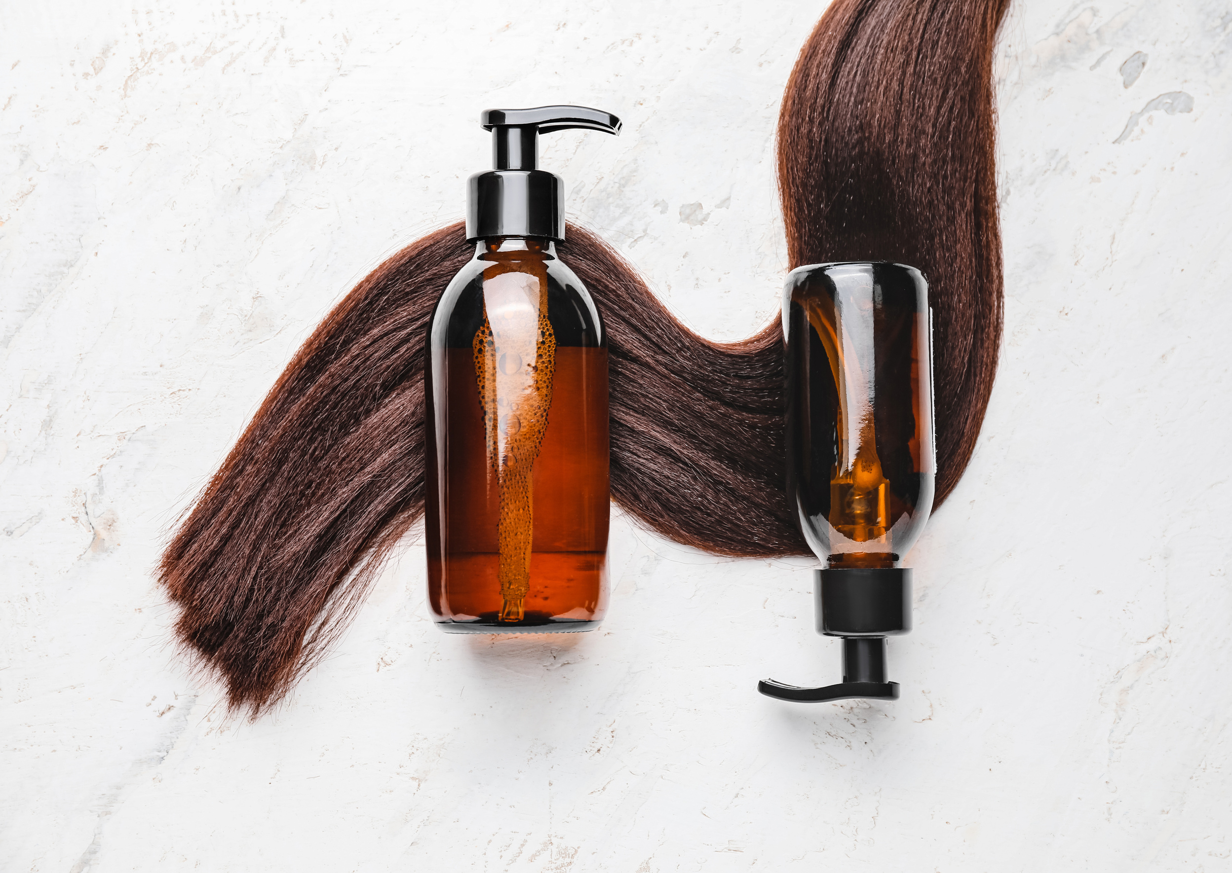 Bottles of Shampoo and Hair Strand on White Background