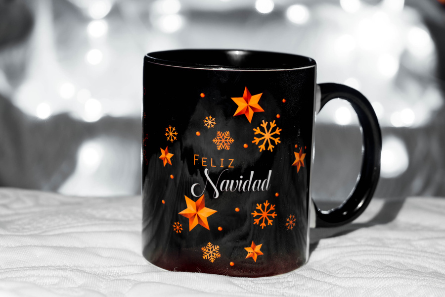 black mug with Christmas decorations on the bed, mug on white cloth, blue background. defocused lights background. christmas concept. sublimation